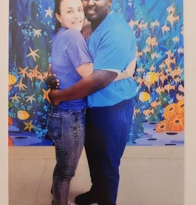 A man and woman embrace in front of a vibrant underwater mural.
