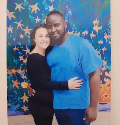 A man and woman posing together in front of a vibrant, starfish-themed mural.