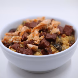 A white bowl filled with a rice bowl recipe featuring chunks of dark meat, shredded salmon, and vegetables.