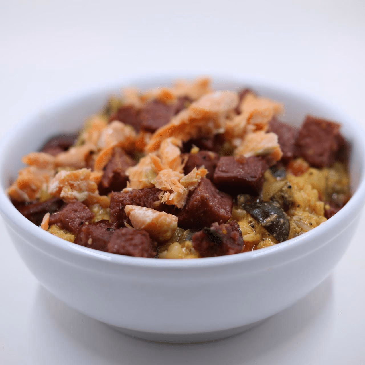 A white bowl filled with a rice bowl recipe featuring chunks of dark meat, shredded salmon, and vegetables.