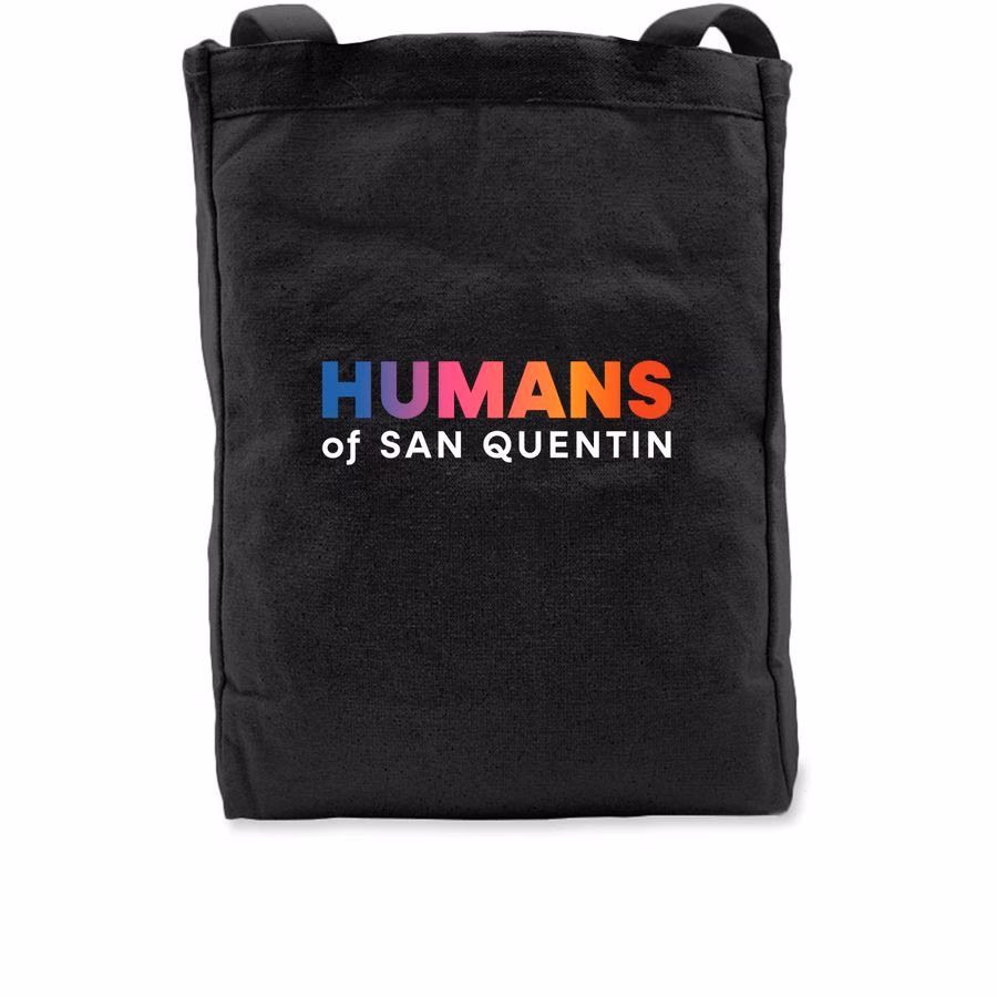 A black tote bag with the text 'HUMANS of SAN QUENTIN' printed on the front. The word 'HUMANS' is in a multi-colored gradient font, while 'of SAN QUENTIN' is in white.