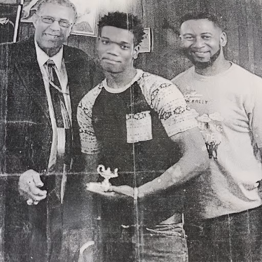 Davontae holds a small trophy between two men in a black and white photo.