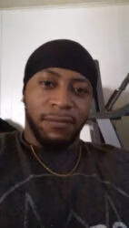 Jarvis Dillard, a man with a beard and a gold chain, wearing a black beanie and a dark t-shirt.