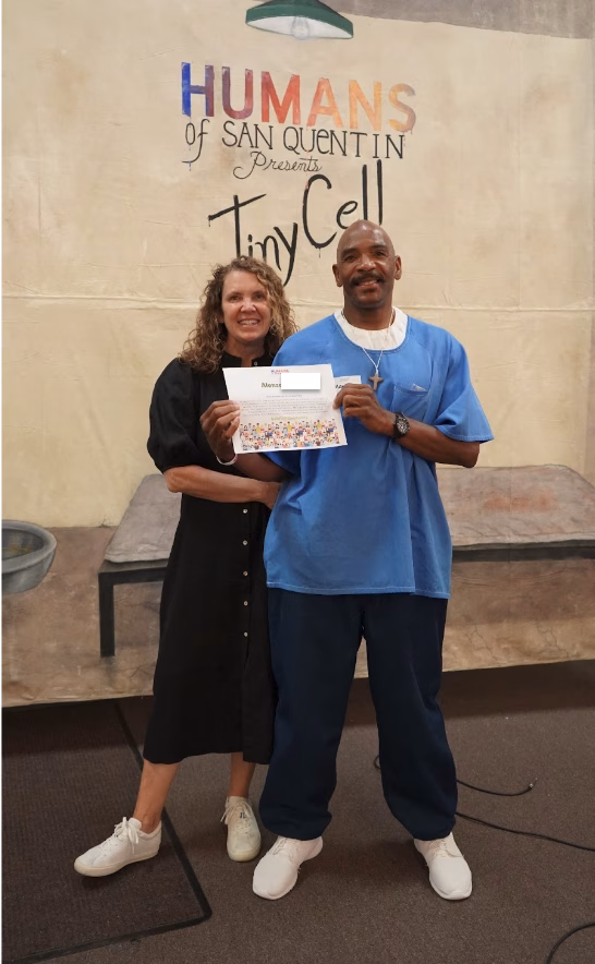 Alonzo, 57, stands with a woman holding a 'Humans of San Quentin' poster in front of a 'Tiny Cell' backdrop.