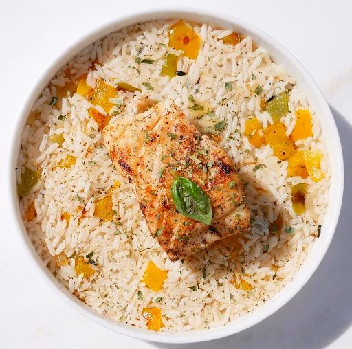 A white bowl filled with rice and vegetables, topped with a piece of seasoned fish and a basil leaf.