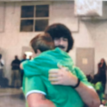 Lucas, 38, embraces another person in a green shirt in an indoor setting.