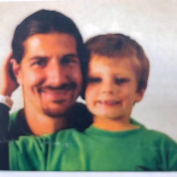 Lucas, 38, smiling with a young boy in a green shirt.