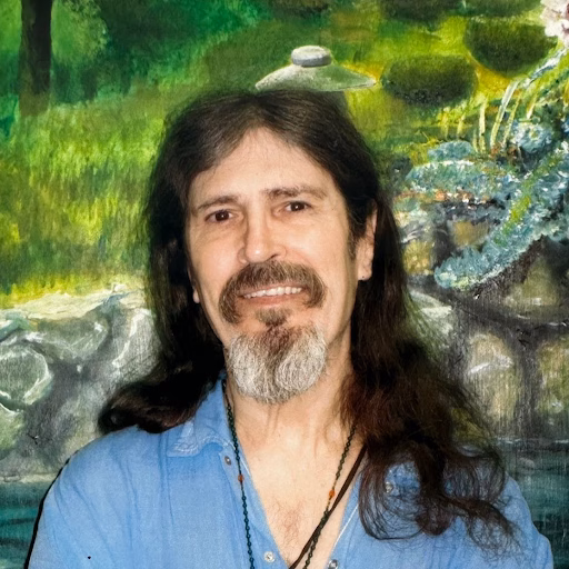 James Snider, a man with long dark hair and a goatee, smiles in front of a green landscape painting.