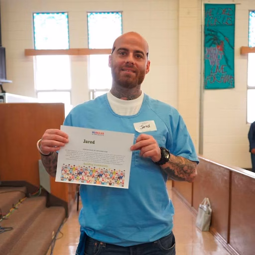 Jared, a man with tattoos and a name tag, holds a certificate from Humane Society of the United States.