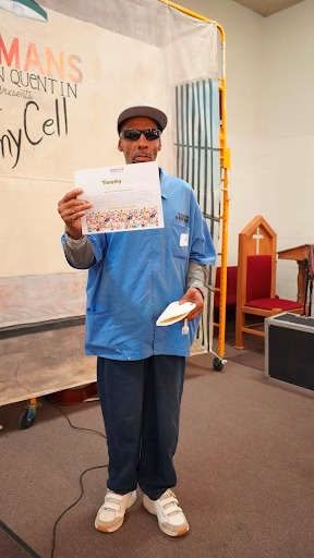 Timothy Ross, 65, holds a certificate in a blue work uniform inside a church.