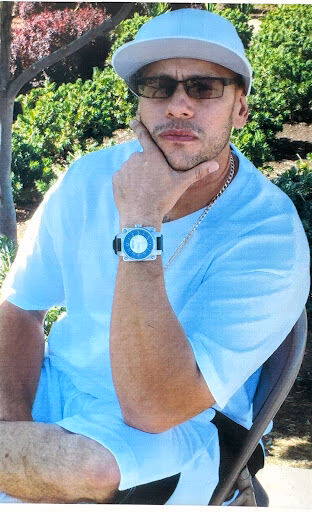 A man named Harold wearing a white cap, sunglasses, and a light blue shirt, resting his chin on his hand while looking at the camera.