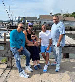 Five people, including a child, pose together on a wooden dock in front of a harbor with boats and buildings.