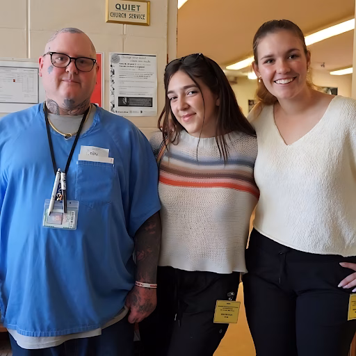 Three people posing together in a hallway. On the left, a man in blue scrubs with a name tag that reads 'Coby'. In the center, a young woman with sunglasses on her head. On the right, a smiling woman in a white sweater.