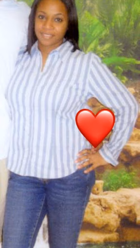A smiling woman in a striped shirt and jeans stands with a hand on her hip, with a red heart emoji covering her torso.