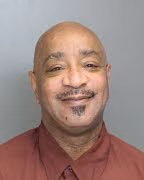 Jeffery, a bald man with a goatee, wearing a red shirt and tie, smiling against a plain background.