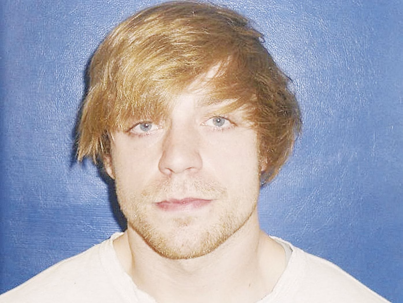 Portrait of Kyle, a man with light brown hair and a light beard, wearing a white shirt against a blue background.