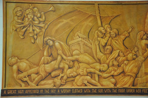 A golden relief mural depicting a dramatic biblical scene with figures in distress, a ship, and angels above, with a descriptive text at the bottom.