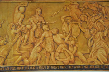 {"alt_text": "A golden-hued relief sculpture depicting a chaotic battle scene with numerous figures in various states of conflict and distress.", "title": "Relief sculpture of battle", "caption": "A detailed relief artwork showing a historical battle scene.", "description": "This image shows a section of a large, golden-hued relief sculpture. The artwork depicts a dynamic and chaotic battle scene with numerous figures engaged in combat. Some figures are shown wielding spears and shields, while others are on the ground, suggesting a fierce struggle. At the bottom of the relief, a partial inscription is visible, reading '...UNDER HER FEET AND ON HER HEAD A CROWN OF TWELVE STARS... THEN ANOTHER SIGN APPEARED IN THE...'}