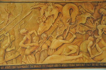 A golden relief sculpture depicting angels fighting a multi-headed dragon, with a caption at the bottom.