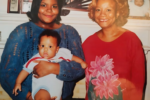 A woman in a blue sweater holds a baby while standing next to an older woman in a red floral shirt.