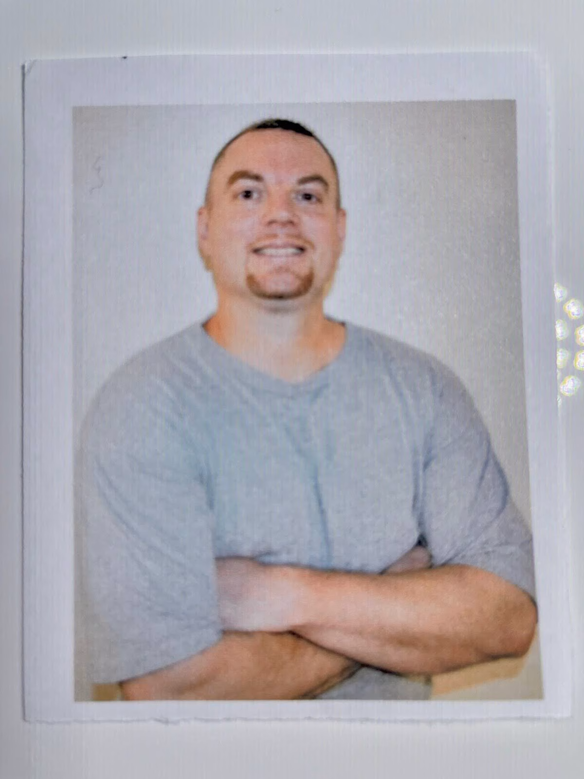 Portrait of Kyle, 40, a man with a goatee and short hair, wearing a grey t-shirt with arms crossed, against a plain background.