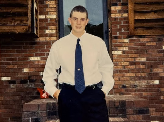 unnamed-6 Kyle, 40, stands on brick steps in front of a brick building with a glass door.