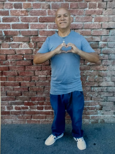 Francisco stands in front of a brick wall, forming a heart shape with his hands over his chest.