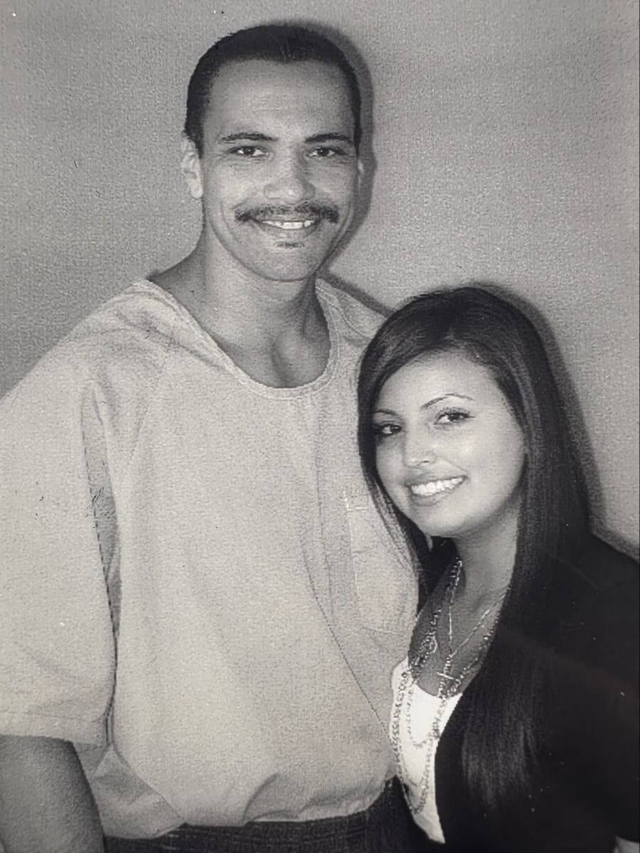 A black and white portrait of a smiling man and woman standing together against a plain wall.