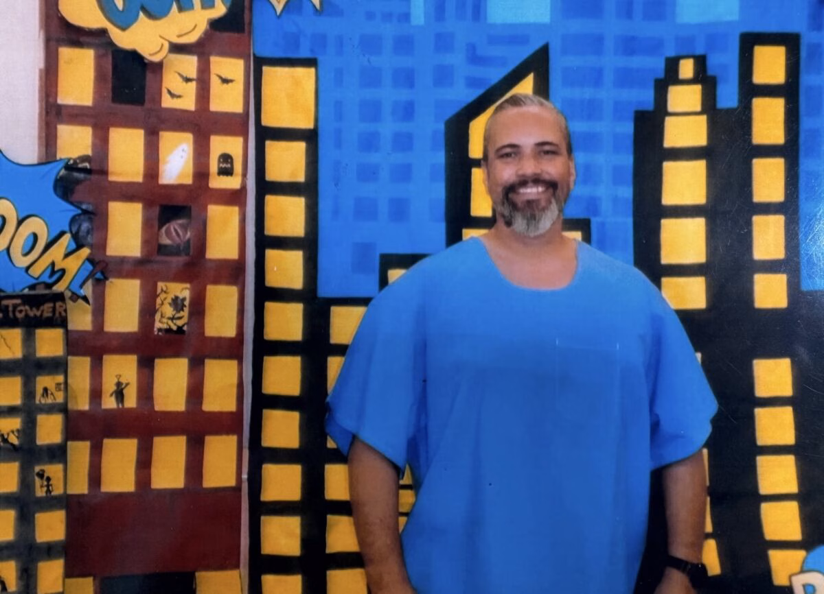 Robert, 51, smiling in front of a colorful comic book cityscape mural.