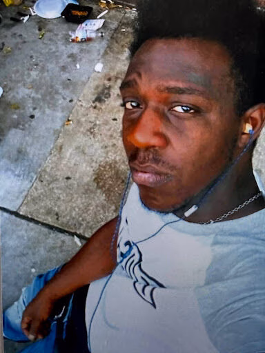 James, a man with dark skin, looking at the camera while wearing a white t-shirt and earphones.