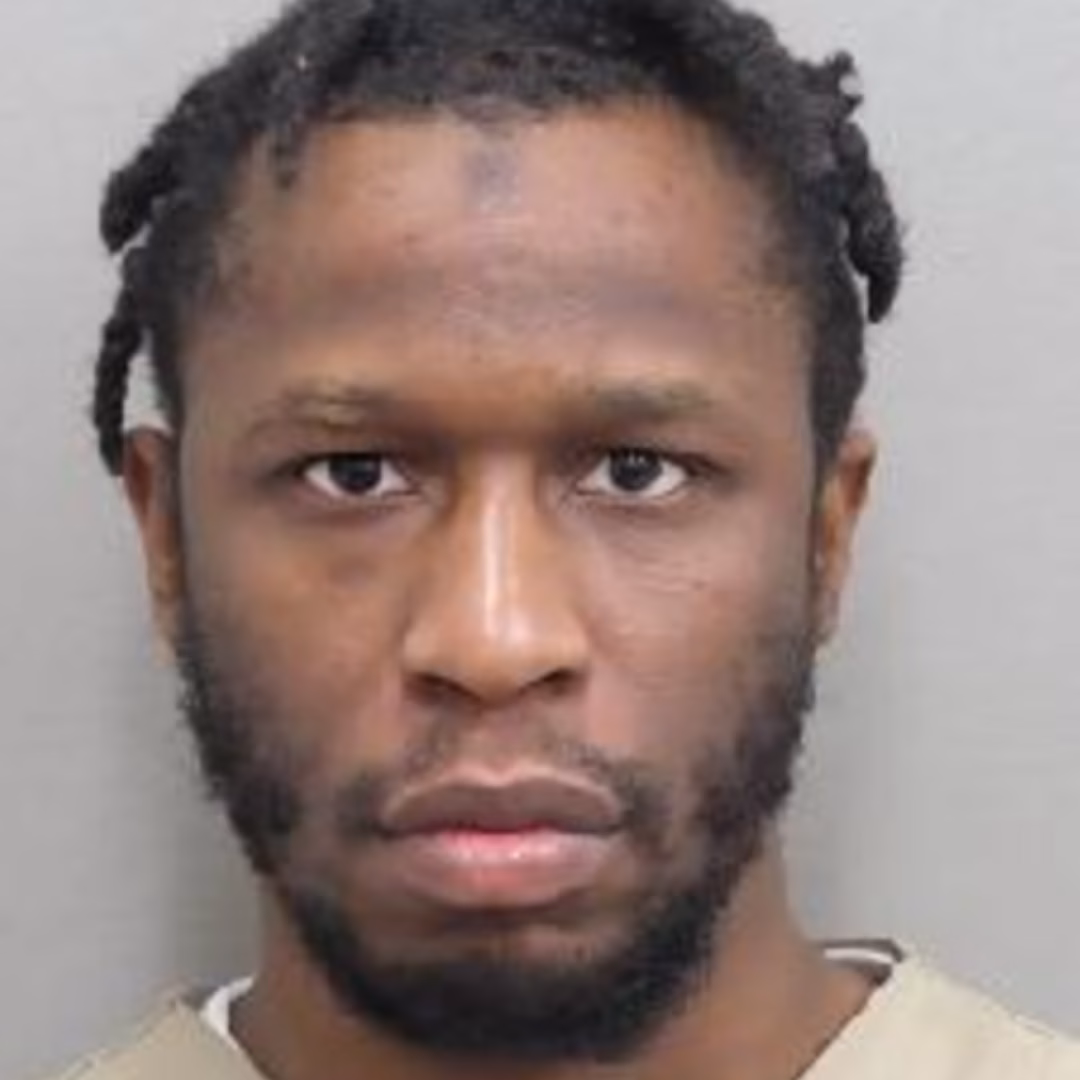 Mugshot of Khalil, a man with a beard and braided hair, wearing a tan shirt.