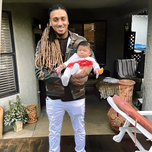 Ray, 32, holding a baby on a porch.