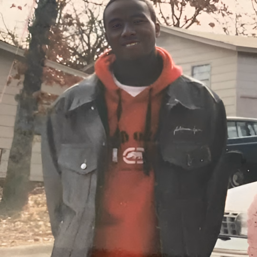 A smiling man identified as Wallace, 45, wearing a red hoodie and a dark jacket, standing outdoors.
