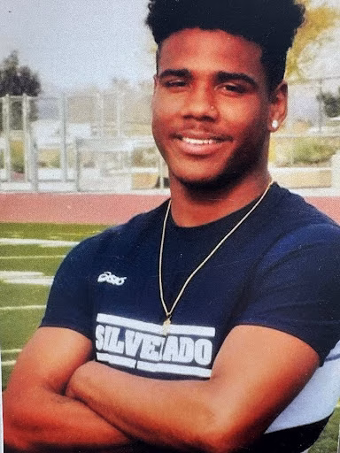 Willie, 23, smiling with arms crossed in a navy blue Silveado t-shirt on a sports field.