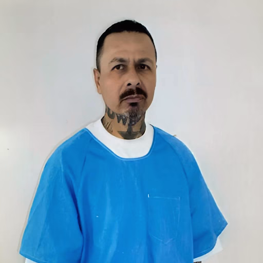 Anthony, a man with a mustache and neck tattoo, wearing a blue salon cape against a white background.