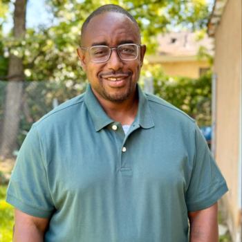 Portrait of Floyd7, a smiling man with glasses and a green polo shirt, outdoors.
