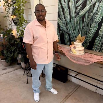 A man named Floyd8 stands in front of a three-tiered cake and a green cactus mural.