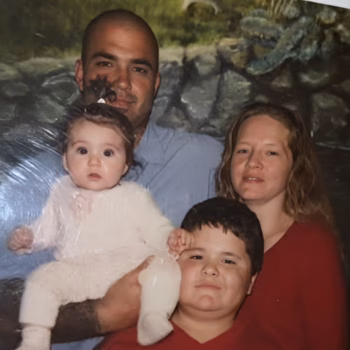 A family of four, a man, a woman, and two children, posing together in front of a nature-themed backdrop.