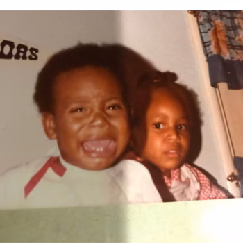 A young boy with his mouth wide open in a joyful expression, standing next to a young girl.