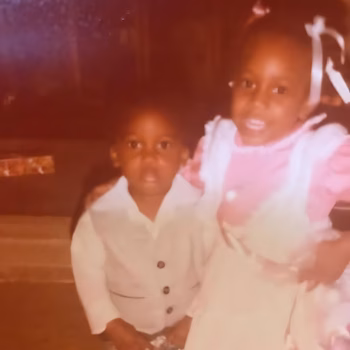 Two young children, a boy and a girl, posing together in a warmly lit, vintage photograph.