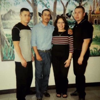 Four people, three men and one woman, standing together in front of a decorative mural.