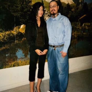 A man and a woman stand together in front of a large mural depicting a mountain landscape.