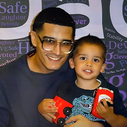 Danny and a young boy pose together, both holding red toy cars, in front of a branded backdrop.