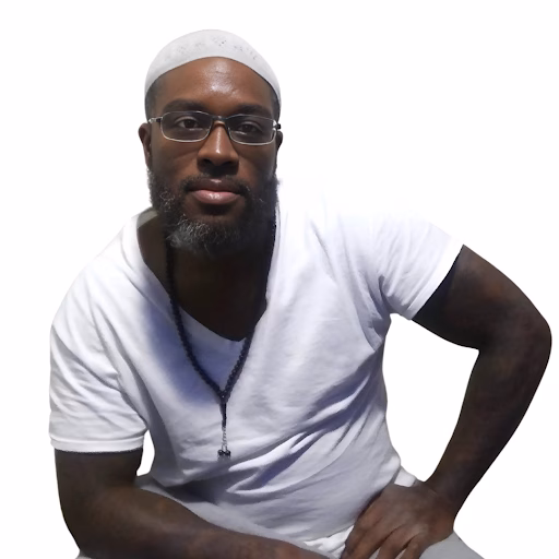 Marcus, a man with a beard and glasses, wearing a white t-shirt and a white cap, poses against a white background.