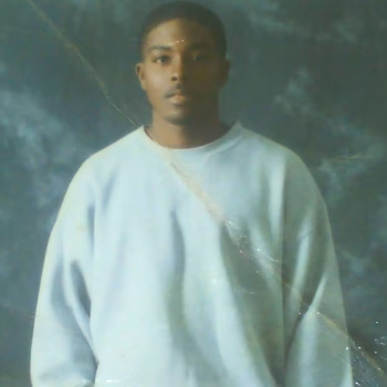 Marcus, a young man with short hair and a light beard, wearing a white long-sleeved shirt against a mottled blue-green backdrop.