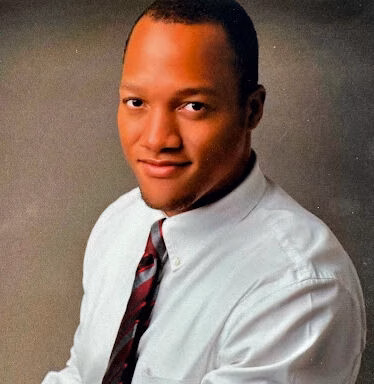 Portrait of Anthony, a man in a white shirt and patterned tie, looking directly at the camera.