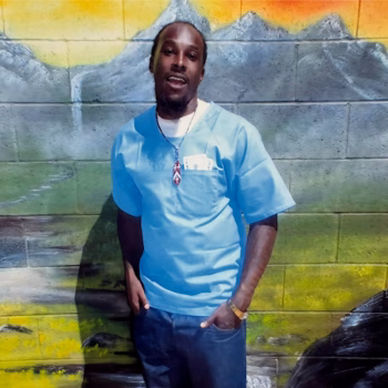 Jasper, 43, stands in front of a mural depicting mountains.