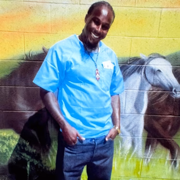 Jasper, 43, smiling in front of a mural of horses.