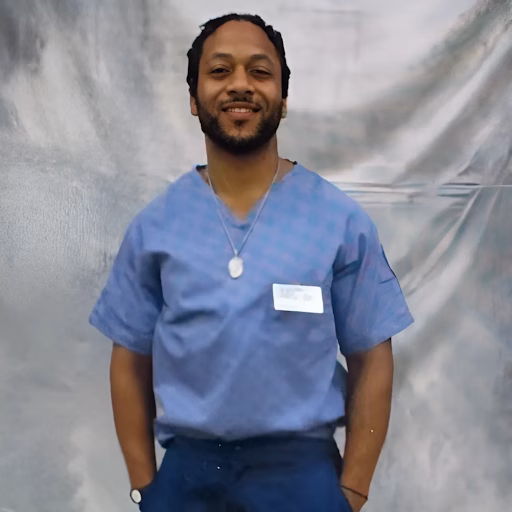 Vernon, 48, smiling in blue scrubs with a name tag.