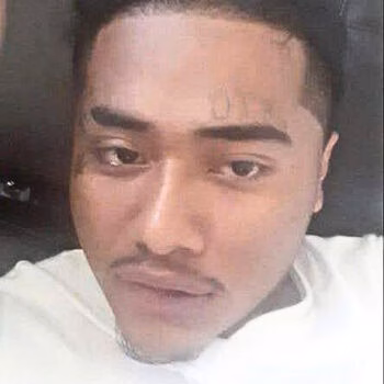Close-up portrait of Kurby, a man with a white t-shirt and a silver chain, looking directly at the camera.